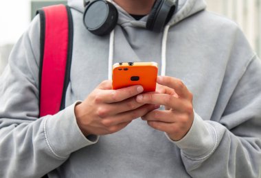 Sırt çantalı, kulaklık takan ve cep telefonu kullanan bir çocuk.