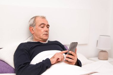 Adam yatakta cep telefonu kullanıyor.