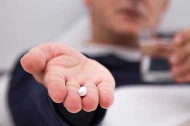 Elinde haplar, kapsüller ve bir bardak su olan bir adam.