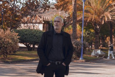 Koyu paltolu bir adam sonbahar manzarasında yürüyor.