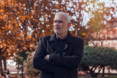 Paltolu ve çapraz kollu bir adam portresi