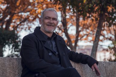 Parktaki bankta rahat rahat oturan ceketli adam.