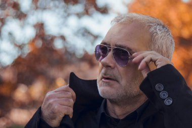 Sonbahar manzarasında ceketli ve güneş gözlüklü bir adam.