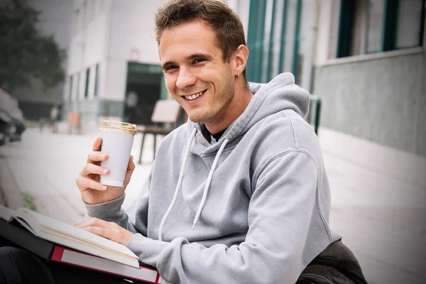 young male student drinking coffee while studying outside the institute
