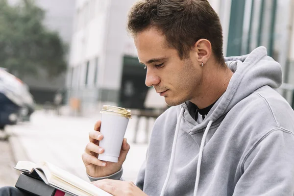 young male student drinking coffee while studying outside the institute