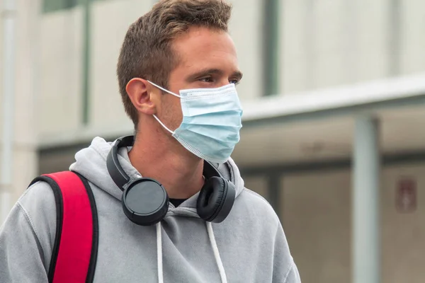 young male student with medical mask and headphones on his way to university or institute