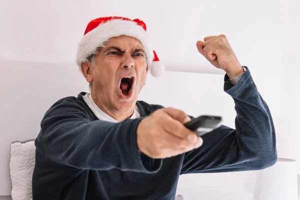 screaming man with victory gesture with santa hat and tv remote control