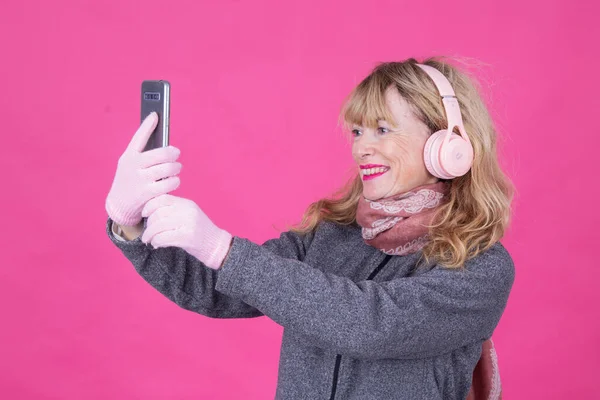 woman with headphones and mobile phone on pink background