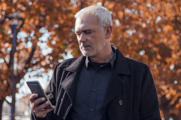 man in coat using his mobile phone on autumn background