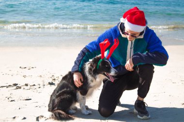 Noel Baba şapkalı bir adam ve onun sınır köpeği sahilde Noel 'i kutluyorlar.