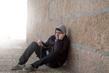 Ceketli ve şapkalı genç adam telefon ve kulaklıkla müzik dinliyor.