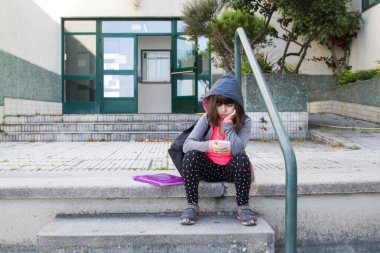 Sırt çantası ve cep telefonu olan öğrenci okul merdivenlerinde oturuyor, okula geri dönüyor.