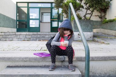 Sırt çantası ve cep telefonu olan öğrenci okul merdivenlerinde oturuyor, okula geri dönüyor.