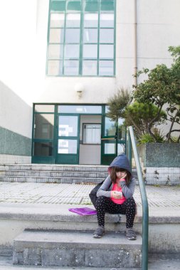 Sırt çantası ve cep telefonu olan öğrenci okul merdivenlerinde oturuyor, okula geri dönüyor.