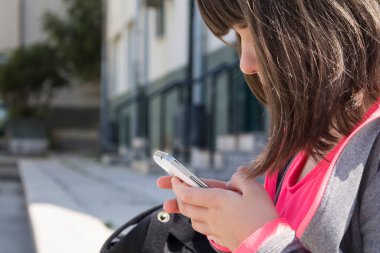 Sırt çantalı öğrenci okulun önündeki cep telefonunu kontrol ediyor.