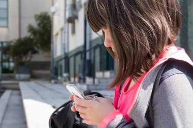 Sırt çantalı öğrenci okulun önündeki cep telefonunu kontrol ediyor.