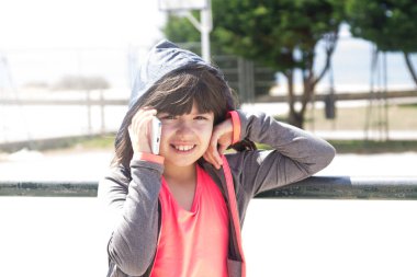 Sweatshirt giyen kız sokakta cep telefonuyla konuşuyor.