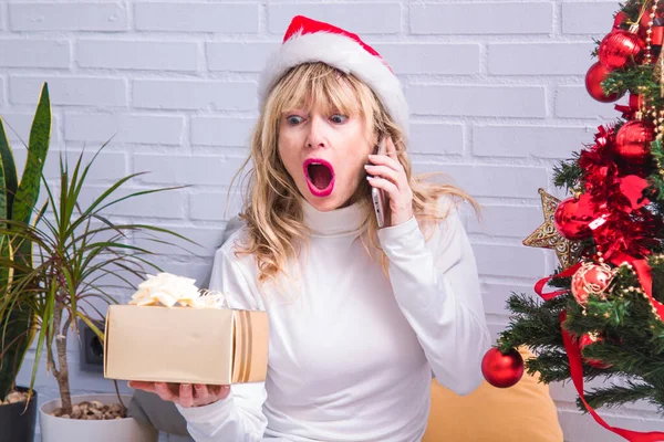 surprised or amazed woman with gift and mobile phone at christmas