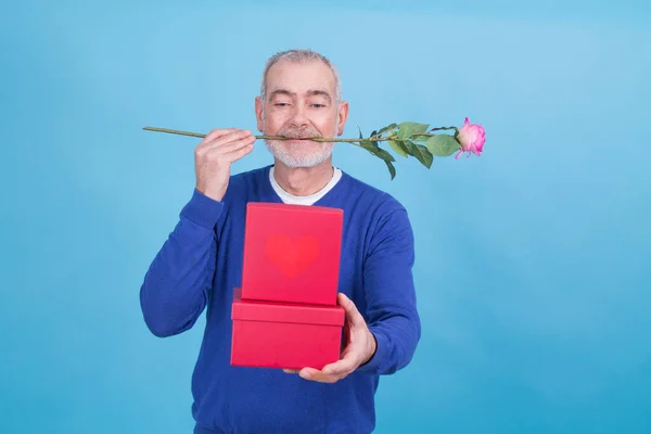 バレンタインデーを祝うために口やギフトボックスにバラと魅力的で面白いシニア男性 — ストック写真