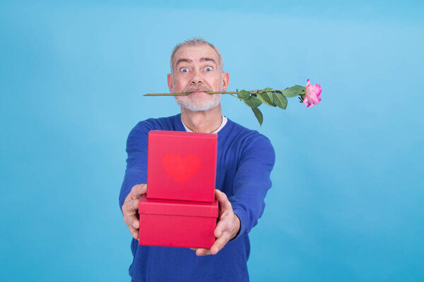 привлекательный и смешной пожилой человек с розой во рту и подарочные коробки, чтобы отпраздновать День Святого Валентина