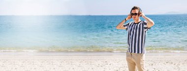 Plajda kulaklıklı rahat bir genç adam.