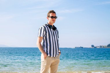 Genç adam plajda kulaklıkla yürüyor.