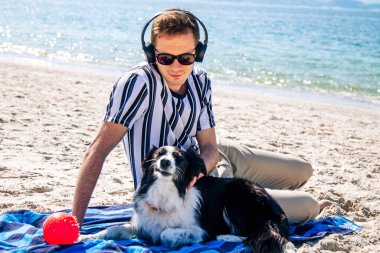  Adam sahilde köpeğiyle eğleniyor ve kulaklıkla müzik dinliyor.
