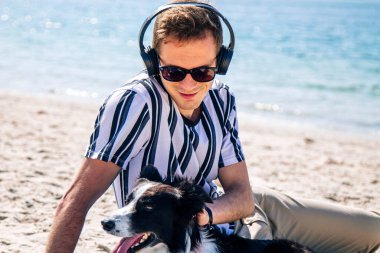  Adam sahilde köpeğiyle eğleniyor ve kulaklıkla müzik dinliyor.
