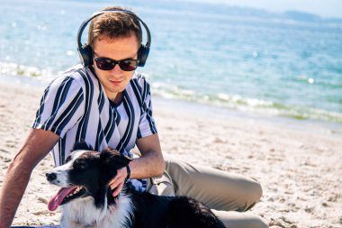  Adam sahilde köpeğiyle eğleniyor ve kulaklıkla müzik dinliyor.