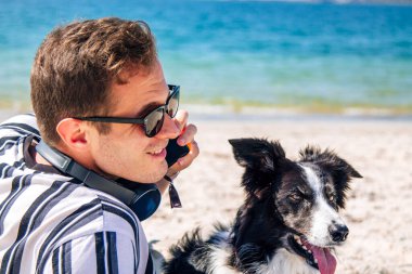 Plajda köpeğiyle cep telefonuyla konuşan genç bir adam.