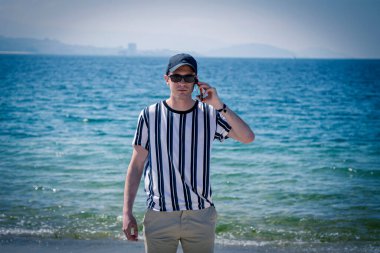 Kumsalda rahat bir adam cep telefonuyla konuşuyor.