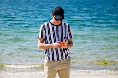 Sahilde cep telefonu kullanan genç bir adam.