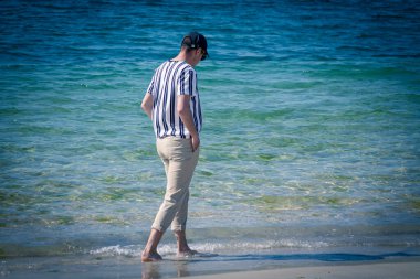 Kumsalda yürüyen rahat bir adam.