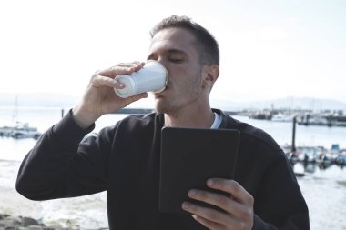 Genç turist dijital tablet kullanıyor ve marinada kahve içiyor.