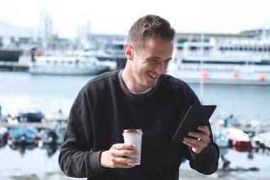 Genç turist dijital tablet kullanıyor ve marinada kahve içiyor.
