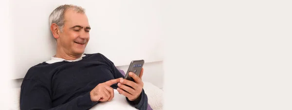 funny man chatting in an app with the mobile phone in bed