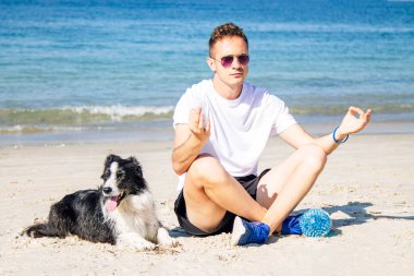 Rahat bir adam köpeğiyle sahilde yoga yapıyor.