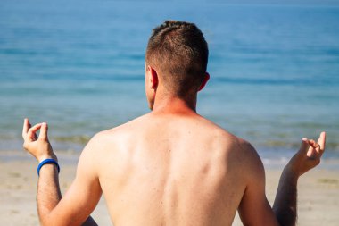 Genç adam plajda yoga yapıyor.