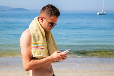 Genç adam sahilde sohbet ediyor ya da telefonla mesaj yolluyor.