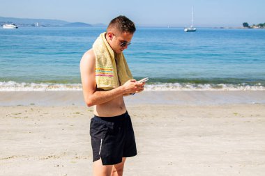 Genç adam sahilde sohbet ediyor ya da telefonla mesaj yolluyor.