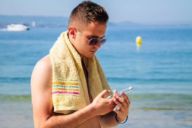 Genç adam sahilde sohbet ediyor ya da telefonla mesaj yolluyor.