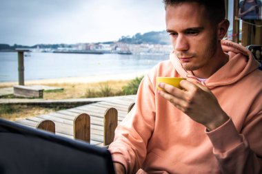 Bir barın terasında dizüstü bilgisayarını kullanan genç bir adam.