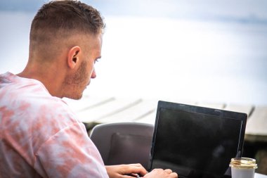 young man in outdoor bar using laptop
