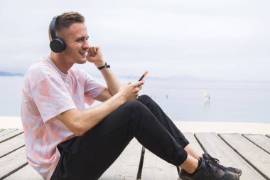 man using mobile phone and listening to music on the beach