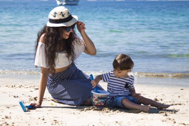 mother with her son playing with the bucket and spade on the shore of the beach