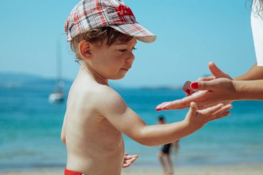 young woman applying suntan lotion on the beach to the child
