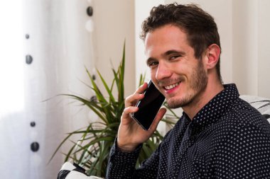 smiling man talking on smartphone at home