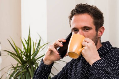 attractive young man having a cup of coffee while talking on the phone