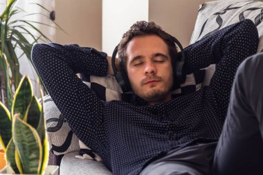 Kulaklıklı genç adam evde müzik dinliyor. Rahatlamak için.