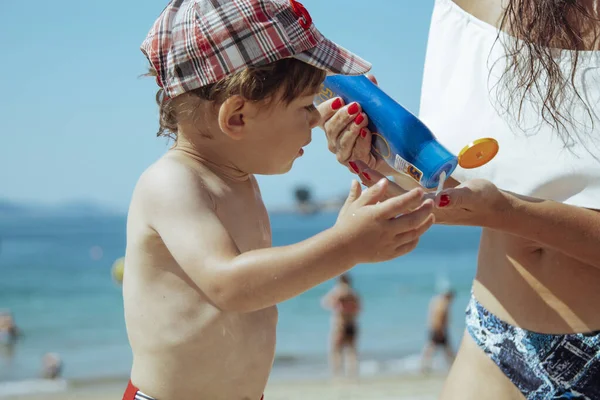 young woman applying suntan lotion on the beach to the child